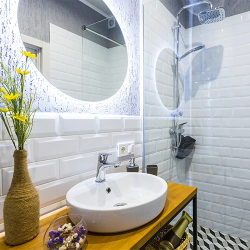 A small bathroom with bright white subway tiles a round backlit mirror and natural elements to enhance brightness and a modern airy feel Castle Bathroom Tile Centre A small bathroom with bright white subway tiles a round backlit mirror and natural elements to enhance brightness and a modern airy feel